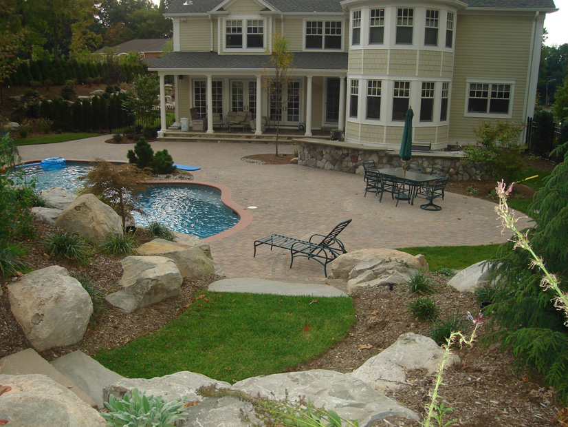 A stone swimming pool is shown in front of a house